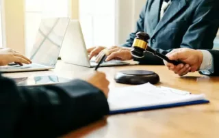 Image of four personal injury lawyers sitting at a table, two with laptops, one signing a piece of pager, and one banging a gavel. You can only see their hands and arms.