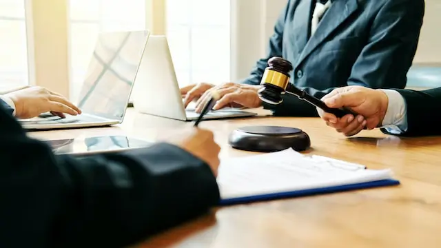 Image of four personal injury lawyers sitting at a table, two with laptops, one signing a piece of pager, and one banging a gavel. You can only see their hands and arms.