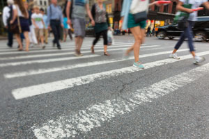 An image of a crosswalk and pedestrians crossing it, with the pedestrians out of focus and a little blurry to denote motion.