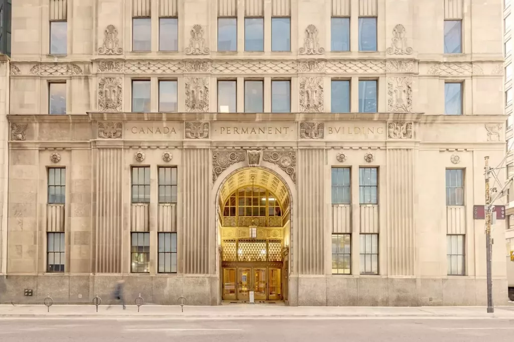 A picture of the front-entrance to the Canada Permanent Trust Building on Bay Street in Toronto, which is a cream marble building with crown molding and a golden entrance.