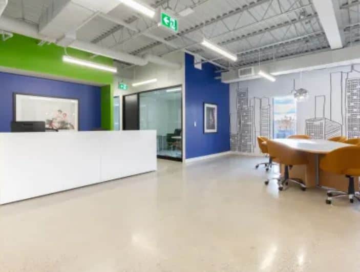Picture of the reception area of the shared workspace in Barrie, featuring a white reception desk, bright green wall, and blue nearby adjoining wall.