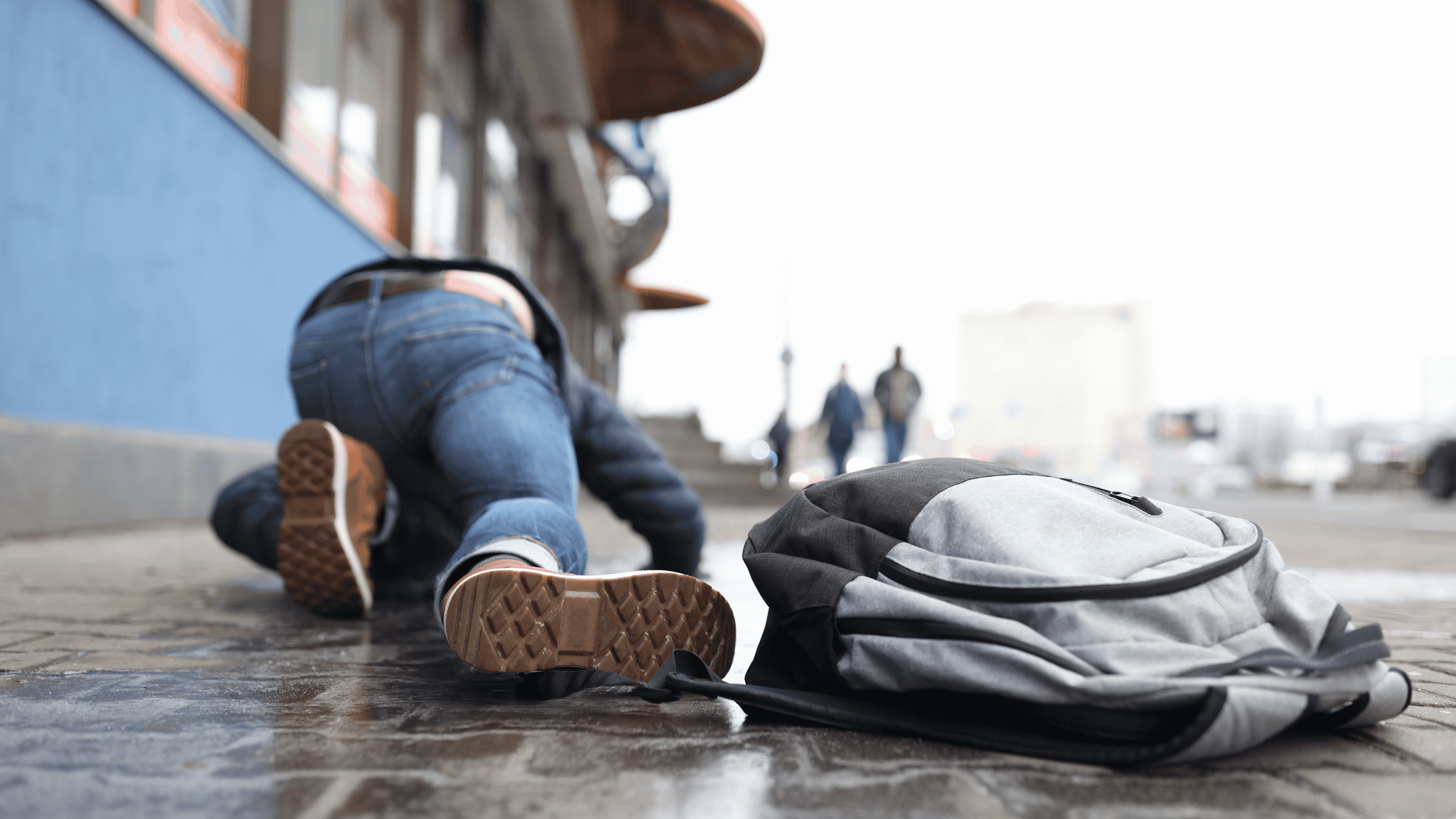 Image of a person who tripped on a city sidewalk, landing on hands and knees and dropping their backpack.